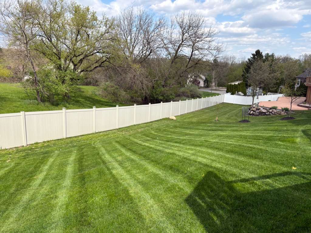 Striped backyard lawn with vinyl fence and rock garden bed by Alfie's Lawn Care Michigan